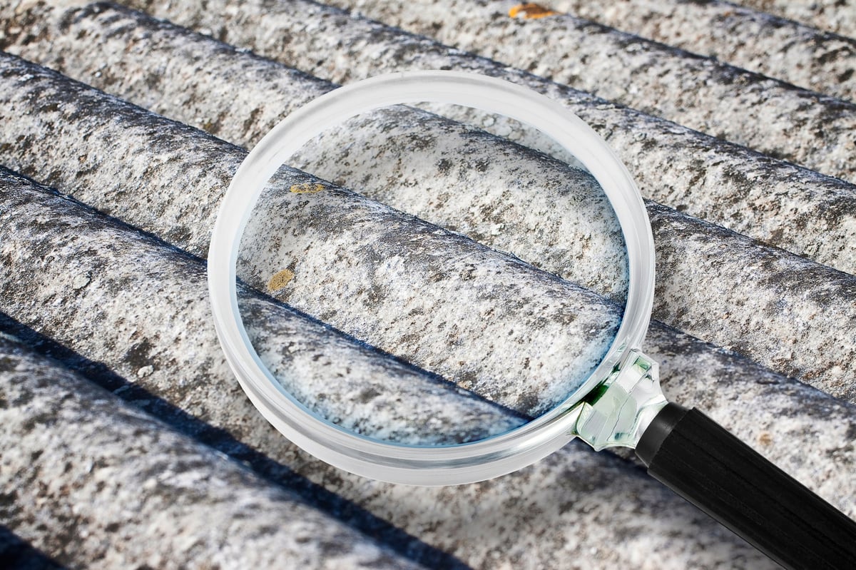 Analysis of the compounds of a dangerous asbestos roof panels - concept image with magnifying glass.