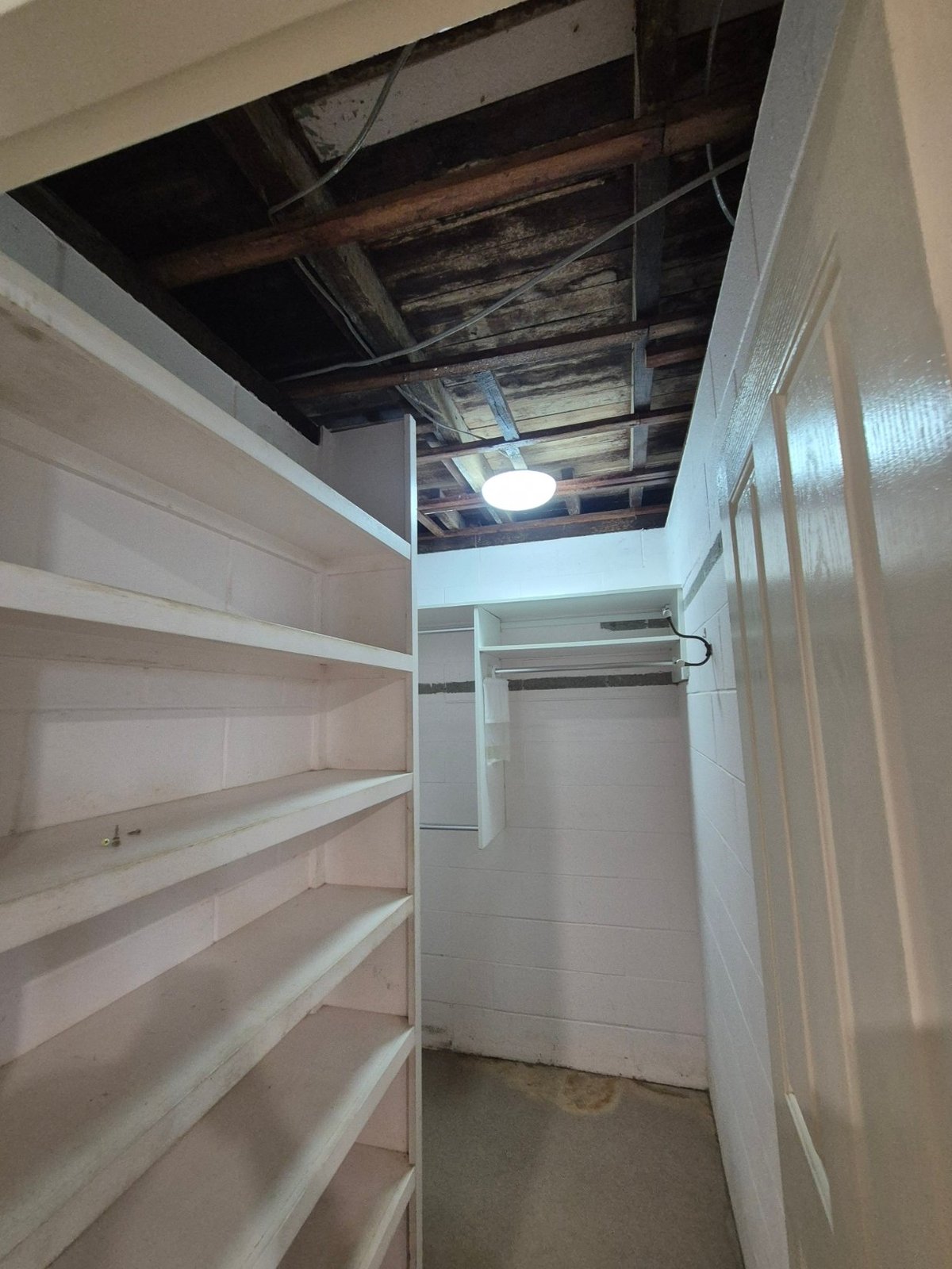 Empty walk-in closet with white shelving, exposed ceiling beams, and open drywall showing interior framing